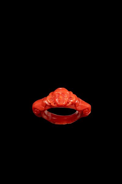 Anello in corallo intagliato, volto entro decorazioni a volute (Italia, XVIII secolo)