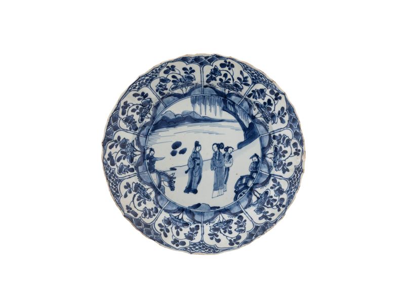 Cina, dinastia Qing (Kangxi), Piatto in porcellana bianca e blu a decoro figurato e cartigli